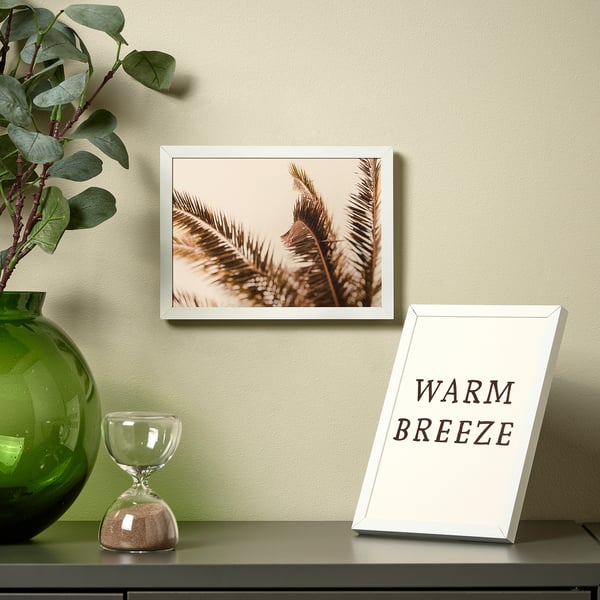 Picture frame on shelf with intricate feather art, surrounded by green vase with plant and hourglass.