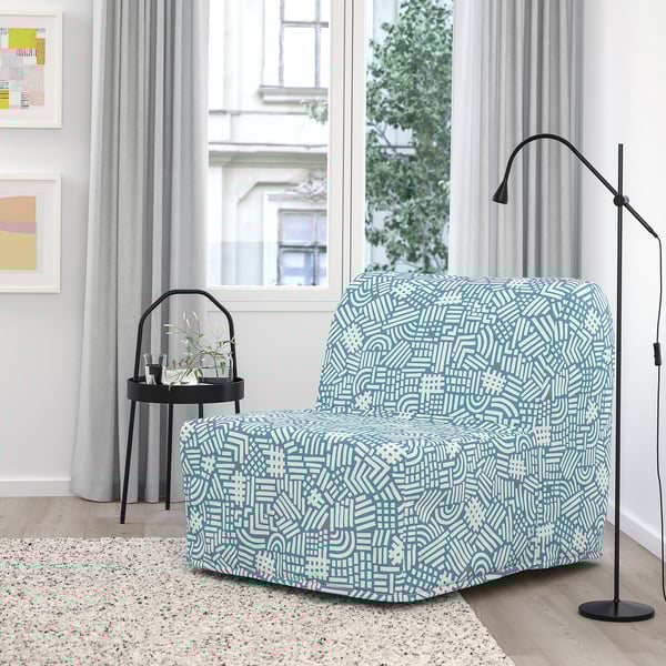 Modern room with blue patterned LYCKSELE LÖVÅS chair-bed, modern lamp, black side table, colorful wall art, and large window.