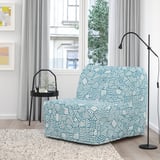 Modern room with blue patterned LYCKSELE LÖVÅS chair-bed, modern lamp, black side table, colorful wall art, and large window.