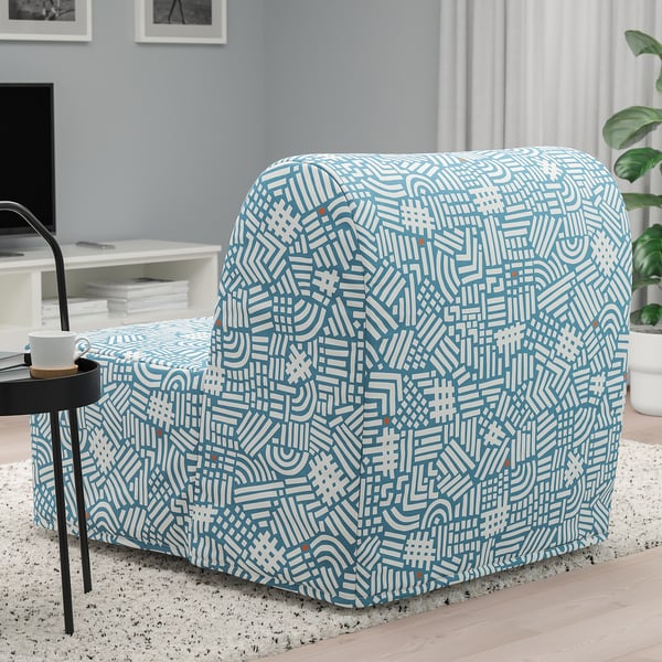 Blue patterned chair with white lines, sitting on rug, next to round table with cup. Converts to bed.