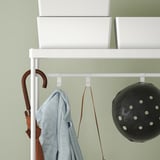 Wall-mounted coat rack with hooks and shelf, holding umbrella and basket.