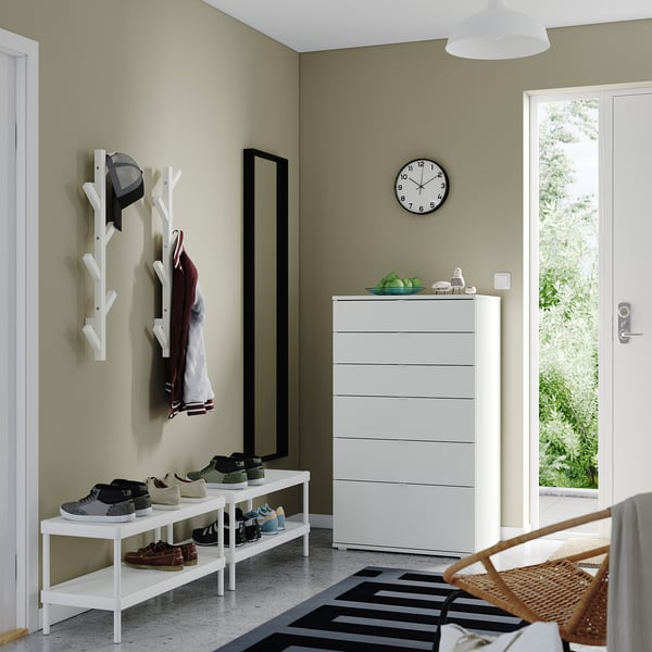 Organized entryway: light green walls, shoe rack, coat hanger, chest with clock, striped rug.