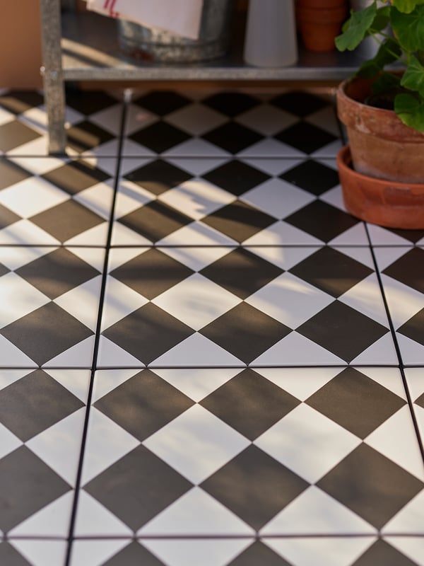 Black and white checkered floor tiles, square shape, outdoor setting with plant.