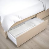 Bed with open drawer, showing storage space. Light wood, white linens.