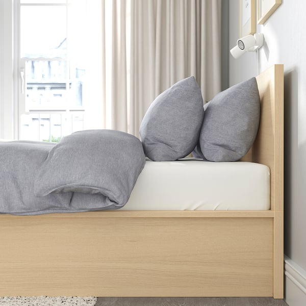 Cozy bed with gray pillows and blanket, wooden headboard, by window.
