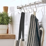 Metal rail with hooks hangs textiles; striped apron displayed.