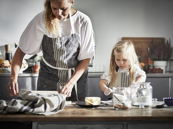 Woman & girl cooking in modern kitchen with striped aprons.