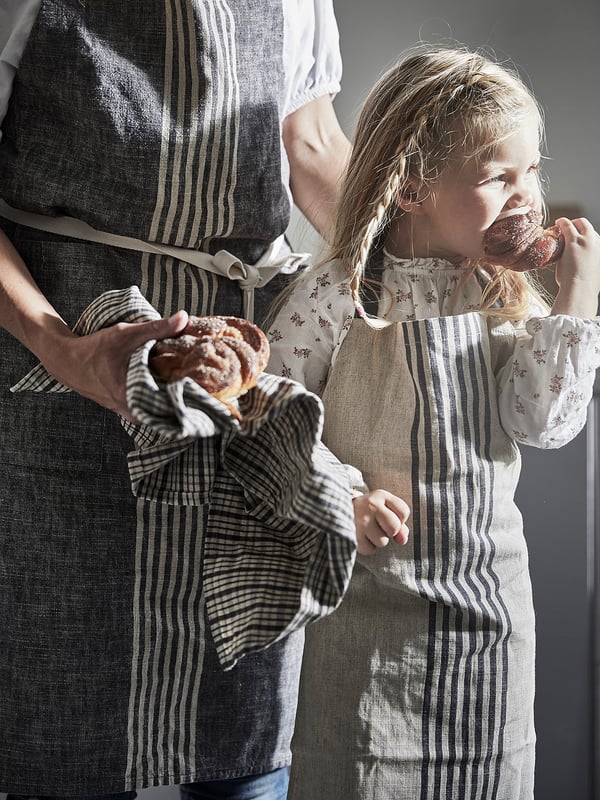 Woman and child baking cinnamon rolls in striped aprons.