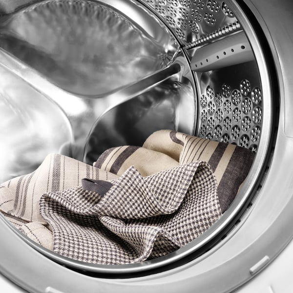 Stainless steel washing machine with front loader filled with MARIATHERES towels, a cotton/linen blend for high absorption.