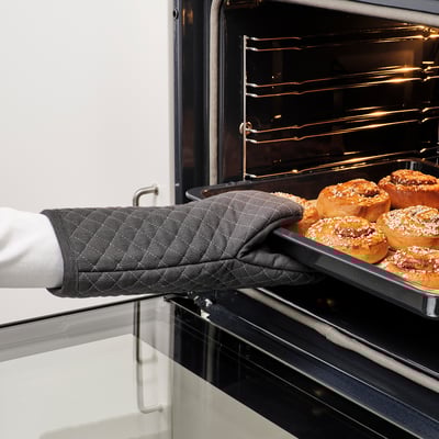 Person using MARIATHERES oven mitt to remove tray of golden-brown pastries from oven.
