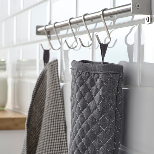 A kitchen area with hanging hooks displaying gray textured oven mitts and a checkered towel, organized for easy access.