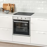 Modern kitchen with stainless steel oven in white cabinets, glass window, wooden cutting board, minimalist white tile backsplash.