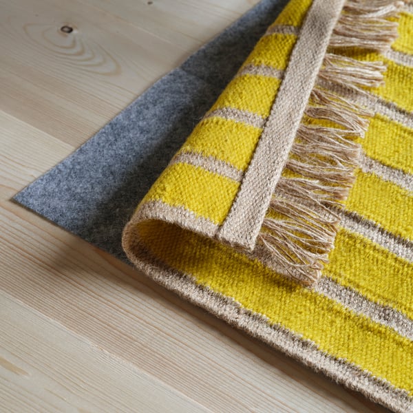 Yellow and beige striped rug with fringe on wooden floor.
