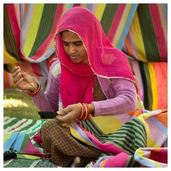 Woman weaving colorful striped fabric. Bright pink headscarf, traditional attire, focused on work.
