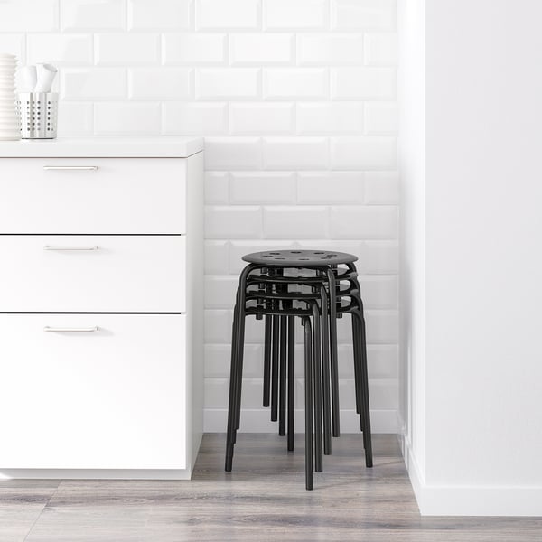 Black stackable stools in kitchen, against white subway tile wall and white cabinets.