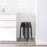 Black stackable stools in kitchen, against white subway tile wall and white cabinets.