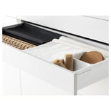 Open kitchen drawer displaying organizer with utensils, including cutlery in paper holder and a cork coaster.