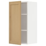 Displays a white METOD kitchen wall cabinet with a single open wooden door, featuring oak veneer and beveled edges.