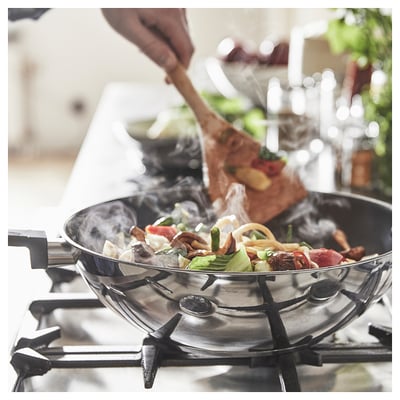 Stainless steel wok cooking colourful veggies on stove, steam rising.