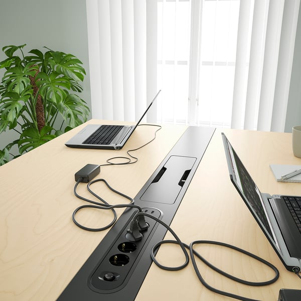 Modern office table with built-in power sockets, neatly organized with laptops, a plant, and a mug.