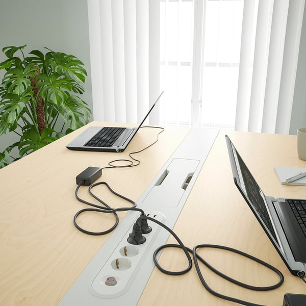 Conference table with cable management, power strips, and laptops. Ideal for meetings, with a footrest for comfort.