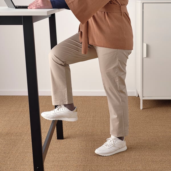 Person standing at high table using laptop, with one foot on footrest.