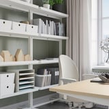 Modern home office with MITTZON white shelving, beige desk, and grey chair. Shelves hold organized files, books, and decor.