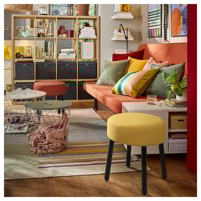 Vibrant living room with orange sofa, colorful pillows, yellow stool, wire table, striped rug, and decorated shelves.