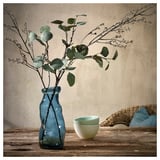 Blue recycled glass vase with green leaves on wooden table.