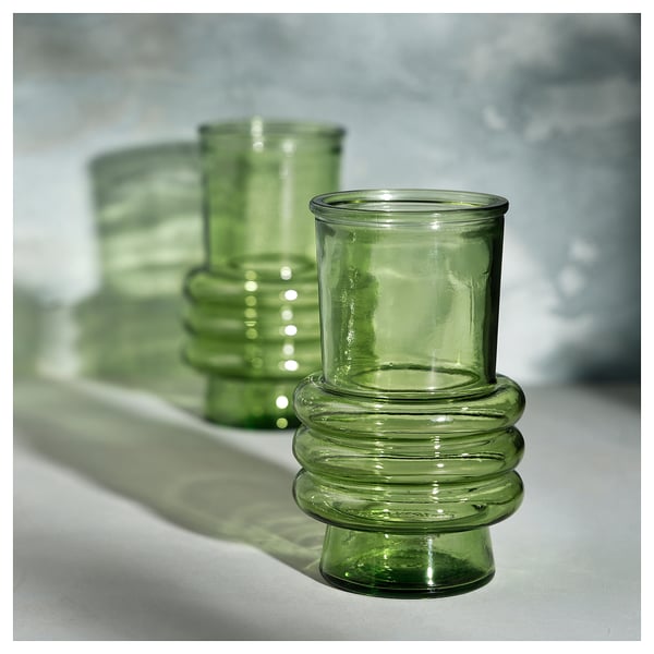 Green recycled glass vase with ribbed design, sitting on a white surface.
