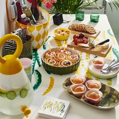 Wooden board with colorful food & drinks. Green tray holds pastries with candles.