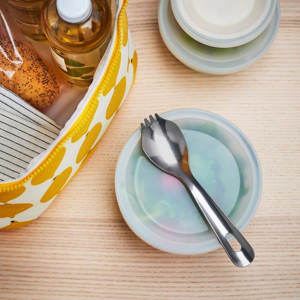 A stainless steel spork, combining spoon and fork in one, sits on a light blue plate. Ideal for travel and outdoor activities.