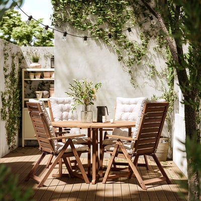 Outdoor patio with NÄMMARÖ table and chairs, cushions. String lights hang overhead, potted plants, white walls.
