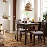 Modern dining setup with dark wooden table, four light beige chairs, pendant lamp, and window with sheer curtains.