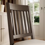Modern farmhouse chair with slatted back and cushioned seat. Dark wood finish, sturdy and padded for comfort.