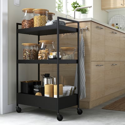 Black 3-tier NISSAFORS kitchen trolley with snacks & items, on casters.