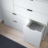 White dresser with open drawer revealing gray fabric contents on light wooden floor.