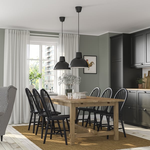 Modern dining room with NORDVIKEN extendable pine table, black chairs, gray wall, black cabinets, and pendant lamps. Seats six.