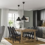 Modern dining room with NORDVIKEN extendable pine table, black chairs, gray wall, black cabinets, and pendant lamps. Seats six.