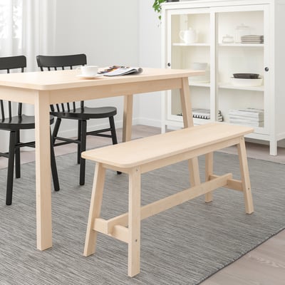 Modern dining setup with light wood table, black chairs, and bench.