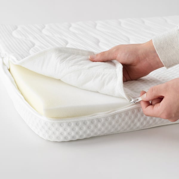 Hands unzipping white mattress pad with soft, plush foam, showcasing its removable, washable cover for easy cleaning.