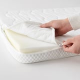 Hands unzipping white mattress pad with soft, plush foam, showcasing its removable, washable cover for easy cleaning.