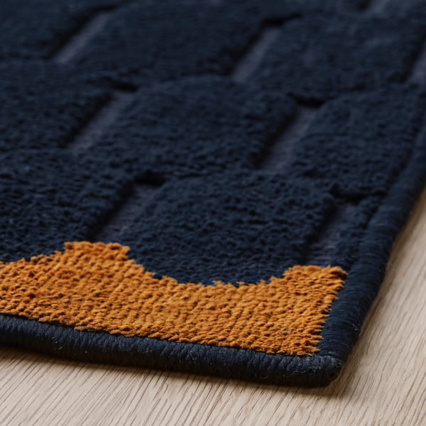 Dark blue and orange patterned rug, laid on wood floor. Thick texture, high quality.