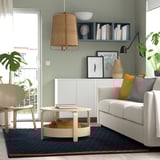 Modern living room with gray sofa, wooden coffee table, and blue rug. Light wood floors.