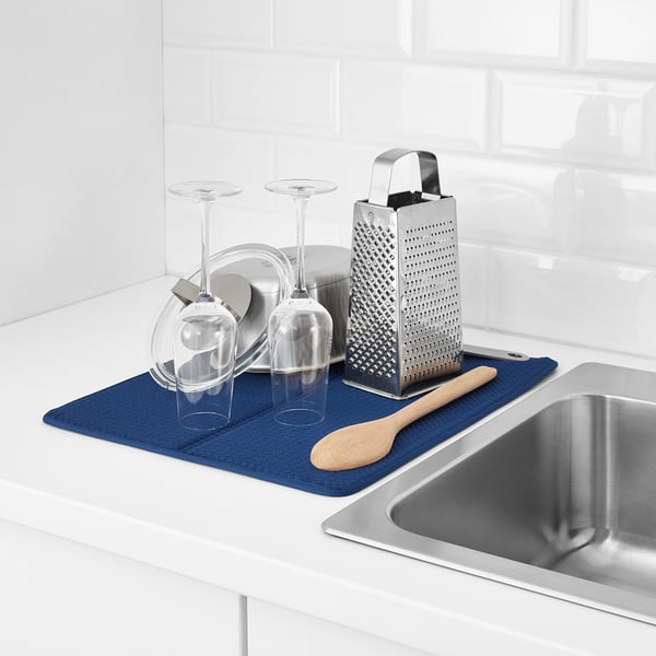 Kitchen counter with wine glasses, plates, grater, spoon, and stainless steel sink. Blue drying mat below items.