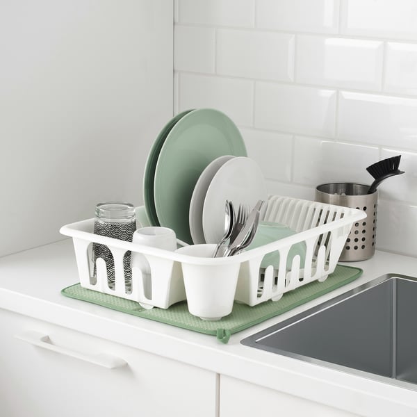 White dish drying rack on kitchen counter with green plates and cups, organized utensils, and a stainless steel container.