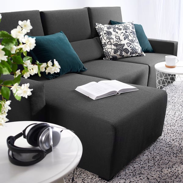 Modern, gray ODENSLUNDA sectional sofa with dark green throw pillows, an open book, and black headphones on a white coffee table near a window.