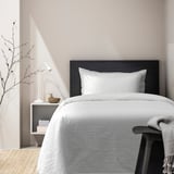 OFELIA VASS duvet set. White, textured cotton. Large bed, wooden frame. Small nightstand, lamp, and decor.