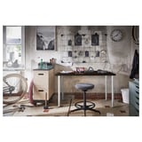 Industrial office setup with OLOV adjustable black desk, contrasting white legs, featuring a chair, bicycle, and wall decorations in a rustic room.
