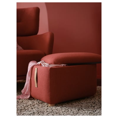 Red fabric footstool with storage, leather handle, and wooden legs in a cozy room.